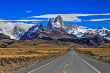 Fitz Roy And Torre Mountains With Route And Cars At Foreground, During A Sunny Day With Clouds.