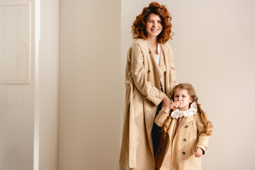 happy mother and cheerful kid standing in trench coats