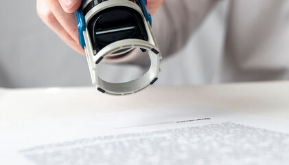 Poster - male hand of a businessman is preparing to put or putting a stamp on documents contract. Signing and stamping contract concept. close up stamp over the document