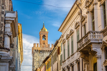 Top of Torre della Pallata brick medieval tower and old buildings with balconies and shutter windows, Brescia city historical centre, blue sky background, Lombardy, Northern Italy