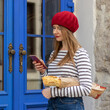 Beautiful woman dressed in French style is holding fresh baguette. In her other hand, a woman holds a smartphone. In the background a beautiful blue door.
