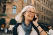 © Maskot - Smiling wrinkled woman talking through phone while looking away in city
