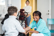 © Maskot - Smiling female nurse shaking hands with boy while mother standing in background at medical clinic