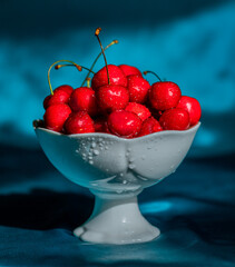 Wall Mural - Red berries with drops of water in a white vase on a blue background. Cherry, fruits. Still life. Food photo.