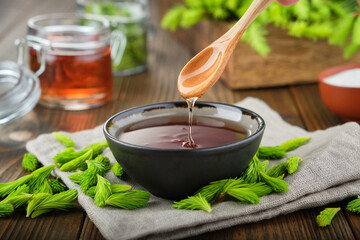 Wall Mural - Cooked syrup or honey from spruce tips in a black bowl, jar of  jam or honey from fir buds and needles, twigs of fir tree on wooden table. Making spruce tips jam at home.