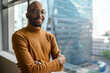 © JonoErasmus - Smiling African businessman standing by office windows overlooking city