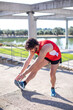 © miguel - Joven runner haciendo estiramientos en el parque después de practicar ejercicio físico