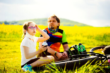 Sport and quarantine. 9 years girl ciclist with father having rest breathing without masks admist the fields in the sunny day