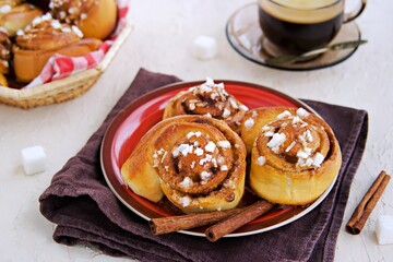 Wall Mural - Swedish twisted cinnamon rolls sprinkled with pearl sugar on a red plate on a light concrete background. Cinnamon pastry