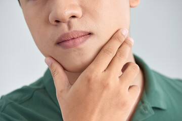 Wall Mural - A close up portrait of young thinking man touching his chin with hand and standing against light grey background. Thinking out loud