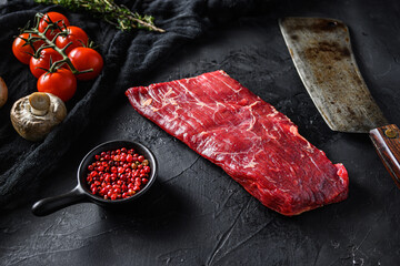 Raw, flap or flank, also known Bavette steak near butcher knife with pink pepper and rosemary. Black stone background. Side view vertical