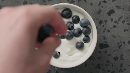 Wall Mural - Slow motion top view blueberries fall into greek yogurt in white bowl on concrete background