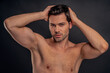 © Roman - Handsome young bearded man isolated. Portrait of shirtless muscular man is standing on grey background and holding his hair.