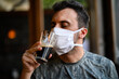 Young man trying to drink a beer wearing a mask, funny coronavirus concept