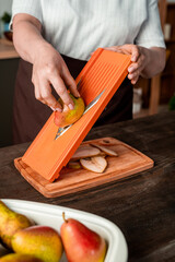 Wall Mural - Casual housewife cutting fresh pears over chopping board by kitchen table