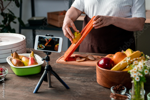 Fotografía Housewife or blogger standing by kitchen table in front of smartphone camera