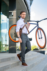 Canvas Print - Contemporary businessman carrying his bicycle while leaving office building