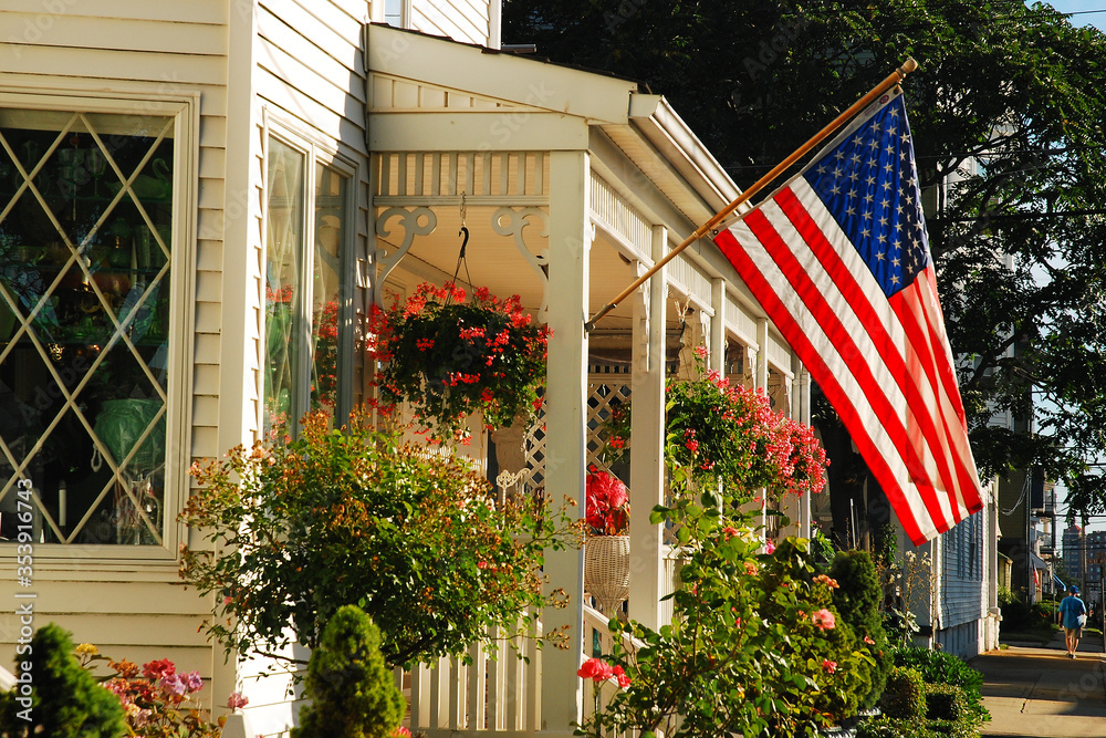 An American flag waves on the front of a home decorated with a small garden - obrazy, fototapety, plakaty 