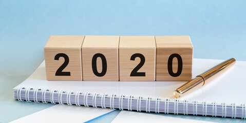 Pay tax in 2020. Wooden cubes with numbers of 2020 year, planner white and pen on blue table.