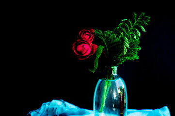 Two red roses and greenery in blue glass vase