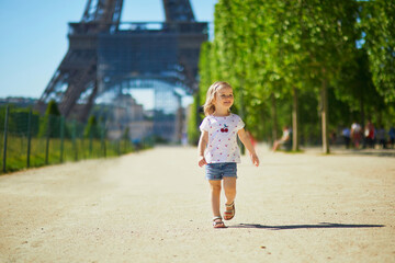 Wall Mural - Cheerful toddler girl running near the Eiffel tower