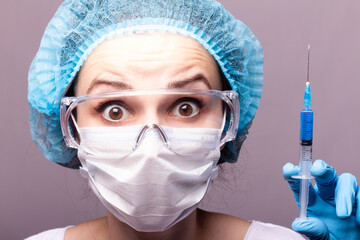 beautiful young girl in medical mask wearing glasses and gloves is holding a syringe with blue liquid