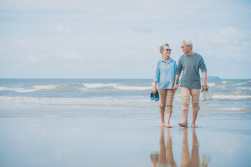 Romantic senior couple while walking hand in hands and talking together at beach..Retirement age concept and love, copy space for text