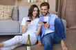 © ty - Happy couple sitting, relaxing on floor in living room, drinking red wine. Smiling young husband and wife rest at home enjoy romantic date on family weekend together