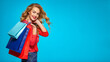 © Valua Vitaly - Happy young woman holds bags with a purchases. Beautiful trendy girl with a colorful shopping bags. Model in a red shirt over blue background holding bags with gifts. Happy caucasian woman.