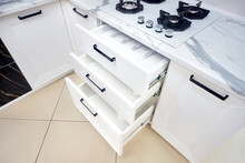 Solutions for placing utensils in modern kitchen - horizontal sliding pullout drawer shelves storage in oak cupboard for kitchenware cookware under stoneware countertop white gas hob with copyspace.