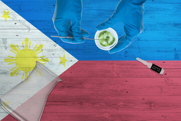 Wall Mural - Philippines flag on laboratory table. Medical healthcare technologist holding COVID-19 swab collection kit, wearing blue protective gloves, epidemic concept.