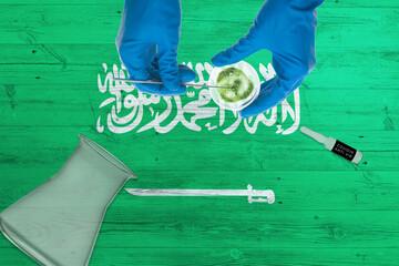 Wall Mural - Saudi Arabia flag on laboratory table. Medical healthcare technologist holding COVID-19 swab collection kit, wearing blue protective gloves, epidemic concept.