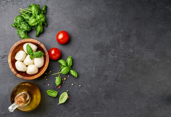 Wall Mural - Ingredients for caprese salad. Red tomatoes, olive oil, fresh herb basil leaves and mozzarella balls over black stone table.