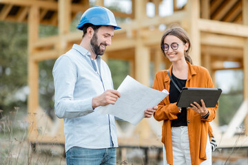 builder with a female client near the wooden house structure on the construction site outdoors. buil