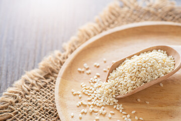 Sticker - White sesame seeds in a wooden spoon on wood table.