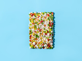 Frozen vegetables assorted on blue background. Assorted frozen vegetables food with ice, top view or flat lay. Raw uncooked frozen hawaii mix. Hard light.