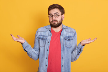 Wall Mural - Image of magnetic handsome helpless young man shrugging with shoulders, looking directly at camera, raising arms, having confused facial expression, wearing casual clothes. Emotions concept.