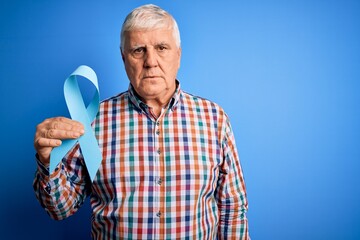 Wall Mural - Senior handsome hoary man holding blue cancer ribbon symbol over isolated background with a confident expression on smart face thinking serious