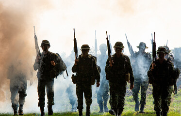 silhouette of unrecognized soldiers with rifle walk through smoke, yellow smoked background. 