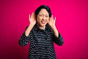 Wall Mural - Young beautiful asian girl wearing casual jacket standing over isolated pink background Trying to hear both hands on ear gesture, curious for gossip. Hearing problem, deaf