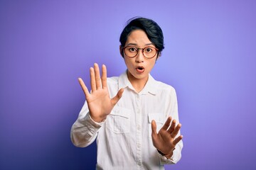 Wall Mural - Young beautiful asian girl wearing casual shirt and glasses standing over purple background Moving away hands palms showing refusal and denial with afraid and disgusting expression. Stop and forbidden