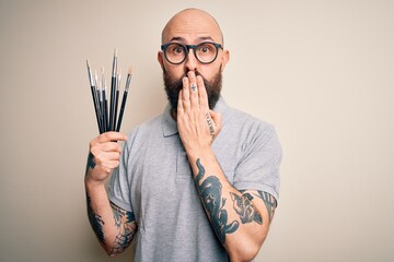 Sticker - Handsome bald artist man with beard and tattoo painting using painter brushes cover mouth with hand shocked with shame for mistake, expression of fear, scared in silence, secret concept