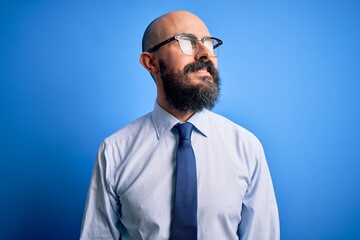 Poster - Handsome business bald man with beard wearing elegant tie and glasses over blue background looking away to side with smile on face, natural expression. Laughing confident.