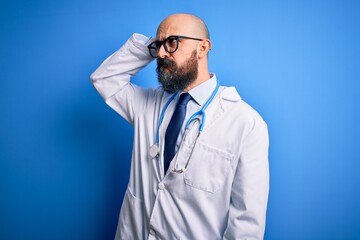 Canvas Print - Handsome bald doctor man with beard wearing glasses and stethoscope over blue background confuse and wondering about question. Uncertain with doubt, thinking with hand on head. Pensive concept.