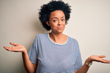 Sticker - Young beautiful African American afro woman with curly hair wearing striped t-shirt clueless and confused expression with arms and hands raised. Doubt concept.