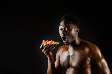 Black handsome naked man eats a pizza. Safety food delivery for people who stays at home. Sexy african man shows 2 pieces of pizza in his hands. Tasty food from pizzeria restaurant