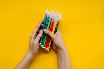 Human hands holding bunch of colorful felt-tip marker pens on a bright yellow background.