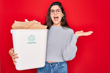 Sticker - Young beautiful woman holding recycle cardboard containter recycling for eco environment very happy and excited, winner expression celebrating victory screaming with big smile and raised hands