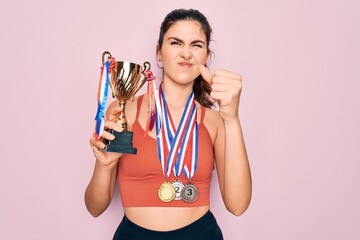 Canvas Print - Young beautiful fitness winner athlete woman wearing sport medals and trophy annoyed and frustrated shouting with anger, crazy and yelling with raised hand, anger concept