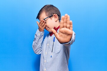 Poster - Cute blond kid wearing nerd bow tie and glasses covering eyes with hands and doing stop gesture with sad and fear expression. embarrassed and negative concept.